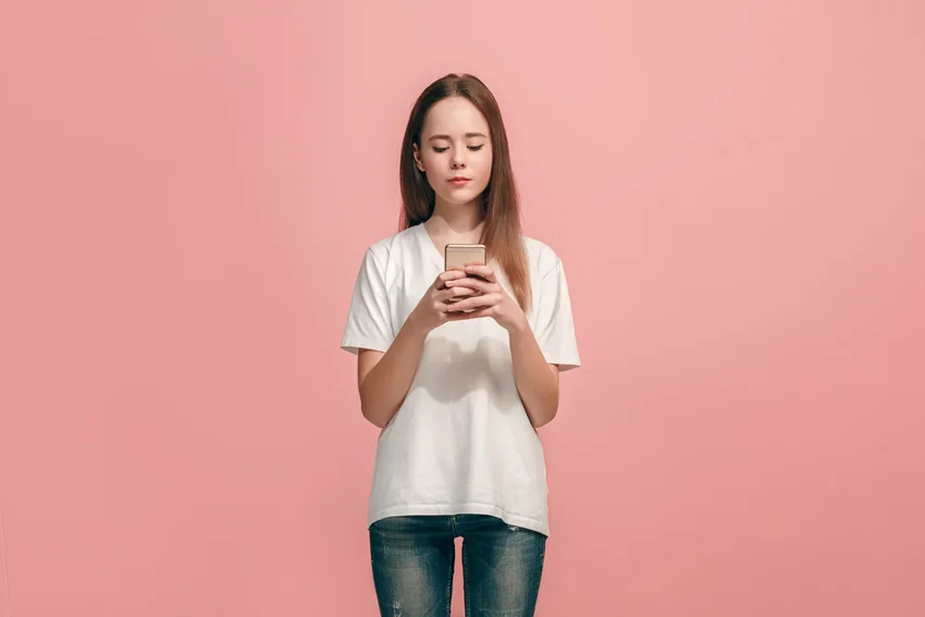Fiatal nő telefonnal rózsaszín háttér előtt